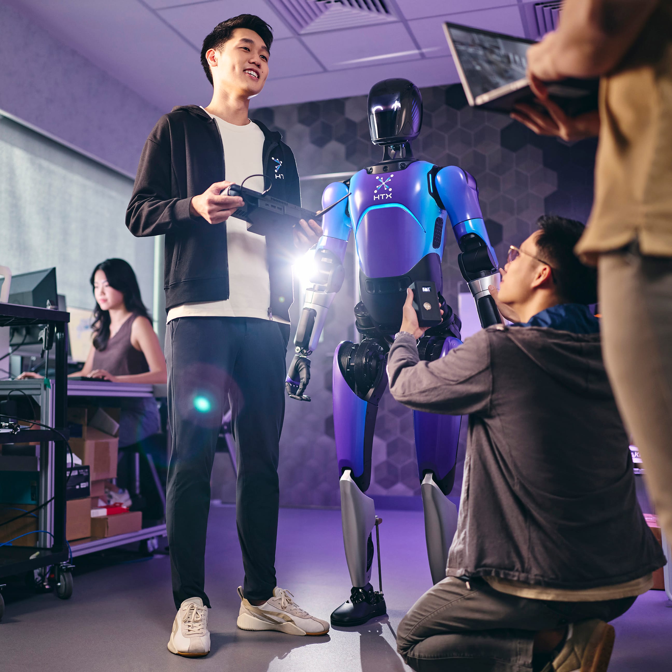 Engineers working on a blue/purple HTX robot with a remote control and laptop in a lab.